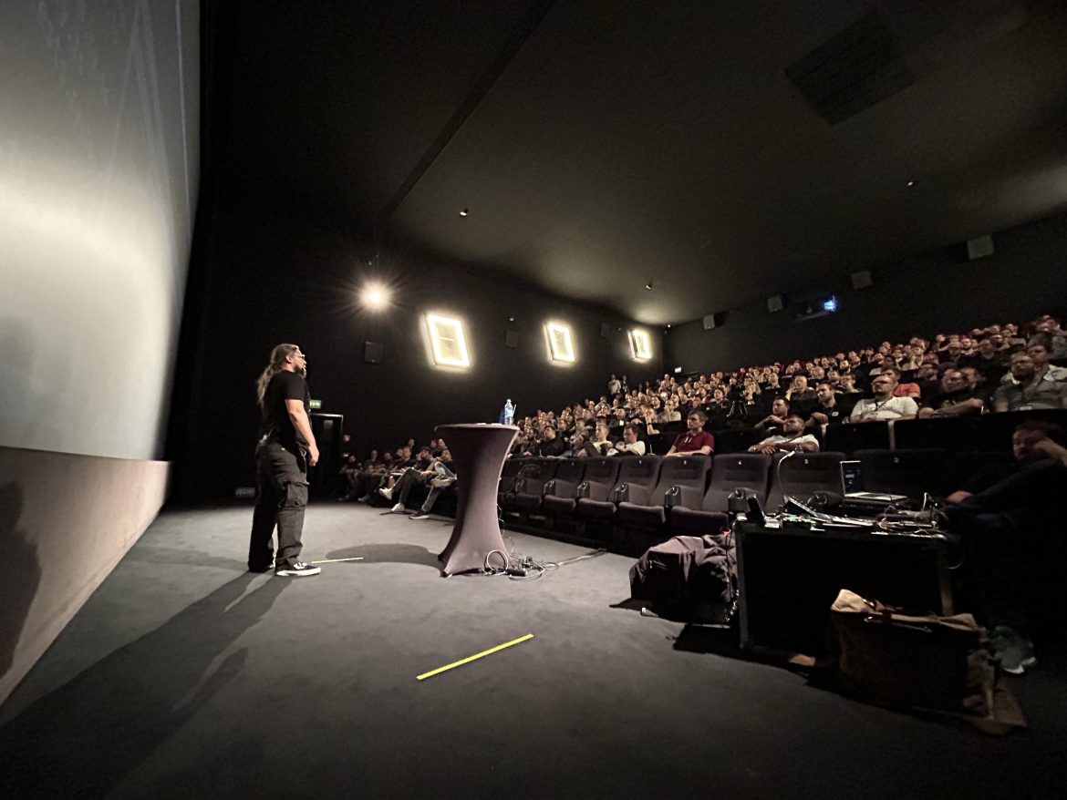 Roland Golla stehend an einem Stehtisch mit Laptop, auf der Bühne der code.talks. Ihm gegenüber sitzt ein bunt gemischtes Publikum.